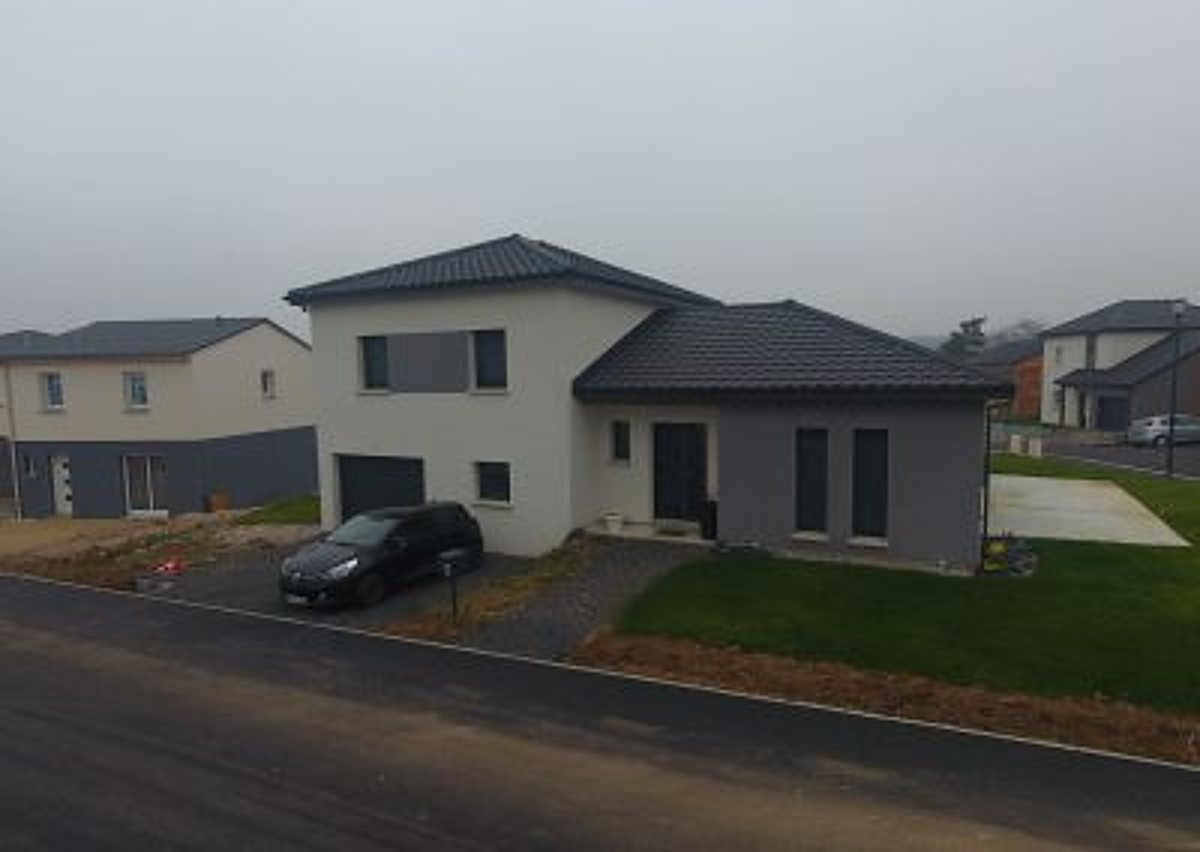 Maison neuve à étage aux façades blanche et grise, avec une voiture noire garée devant, dans un lotissement récent par temps brumeux.